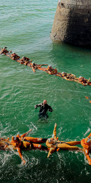 People participating in a water rescue training exercise, linked by life vests.
