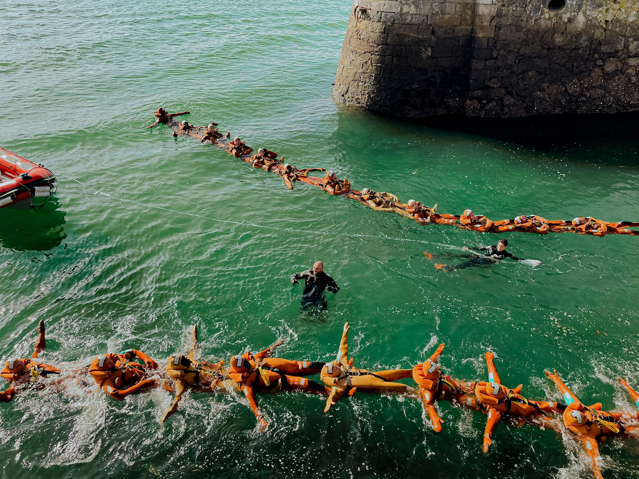 People participating in a water rescue training exercise, linked by life vests.