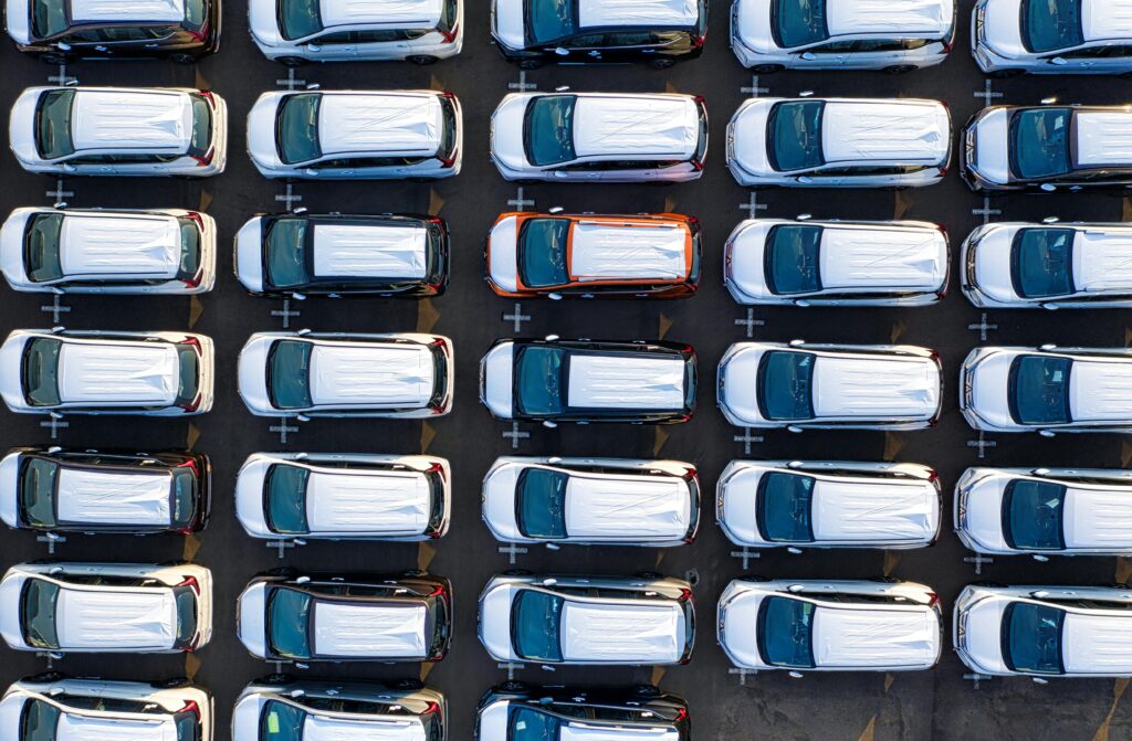 Top view of numerous new cars parked in rows in an urban lot, showcasing modern transportation infrastructure.
