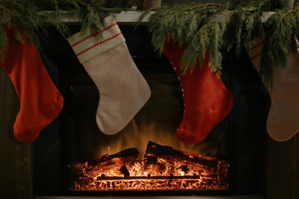 Warm and festive fireplace decorated with hanging stockings and greenery, perfect for the holidays.