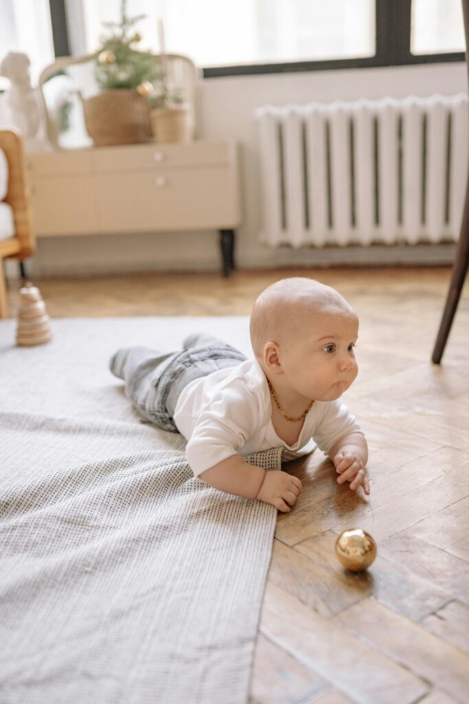 Cute baby crawling on a rug indoors near a golden Christmas ball.