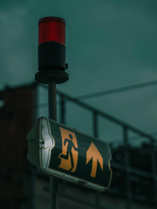 Moody urban scene with exit sign and warning light under a dusk sky.