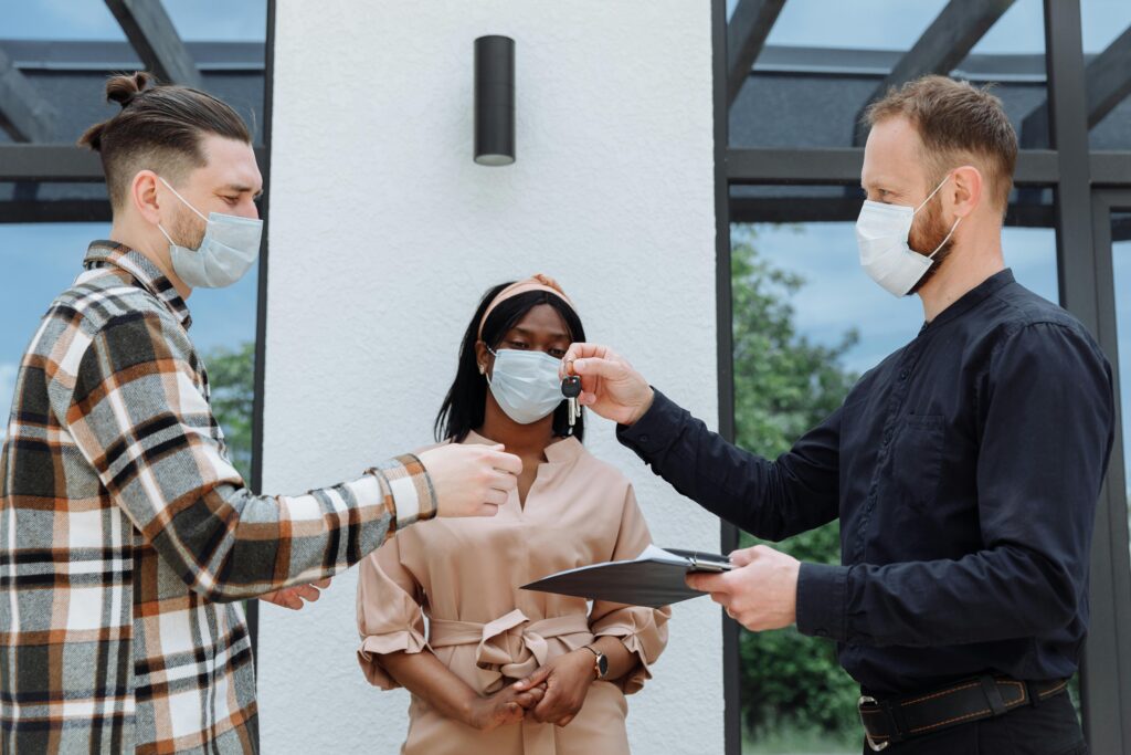 Real estate agent handover keys to a diverse couple wearing face masks, outdoors.